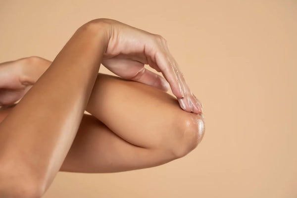 Application d'un soin nourrissant sur une peau sèche du corps, gros plan sur le coude, lumière naturelle chaude
