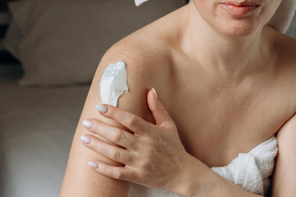 Femme appliquant un sérum corps nourrissant sur son épaule après la douche, lumière naturelle chaude
