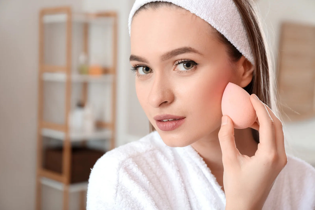 Femme appliquant une CC crème teintée à l'éponge pour un teint naturel unifié