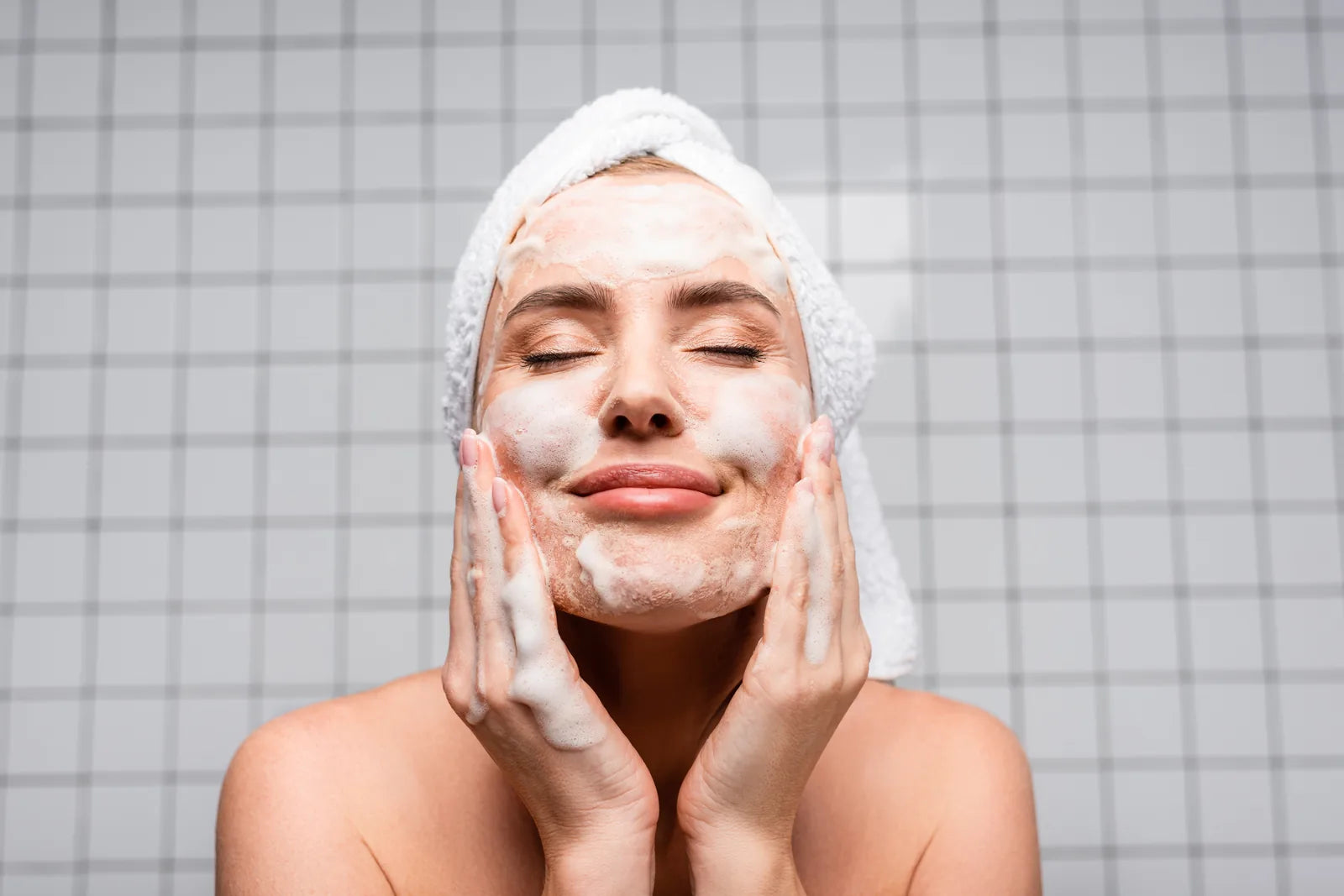 Femme appliquant un nettoyant moussant sur son visage dans une salle de bain — geste du double nettoyage