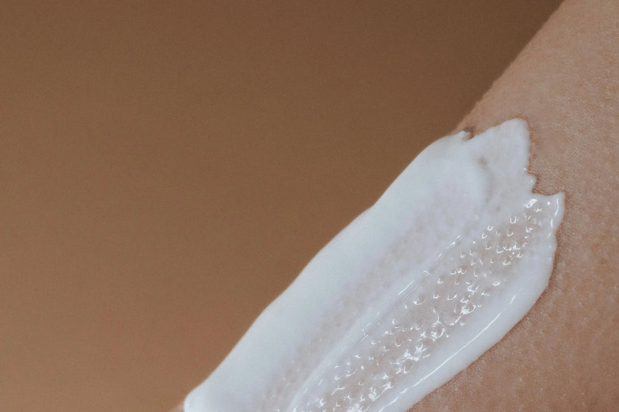 Touche de crème blanche étalée sur la peau d'un avant-bras, fond brun chaud — CAMENYS