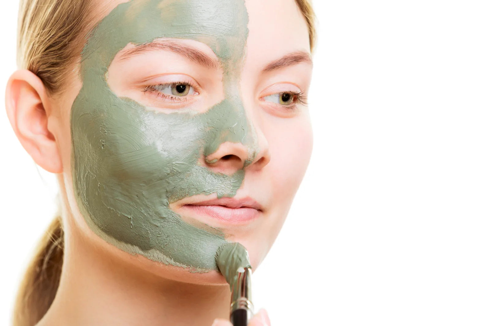 Femme appliquant un masque à l'argile sur le visage au pinceau, geste de soin purifiant