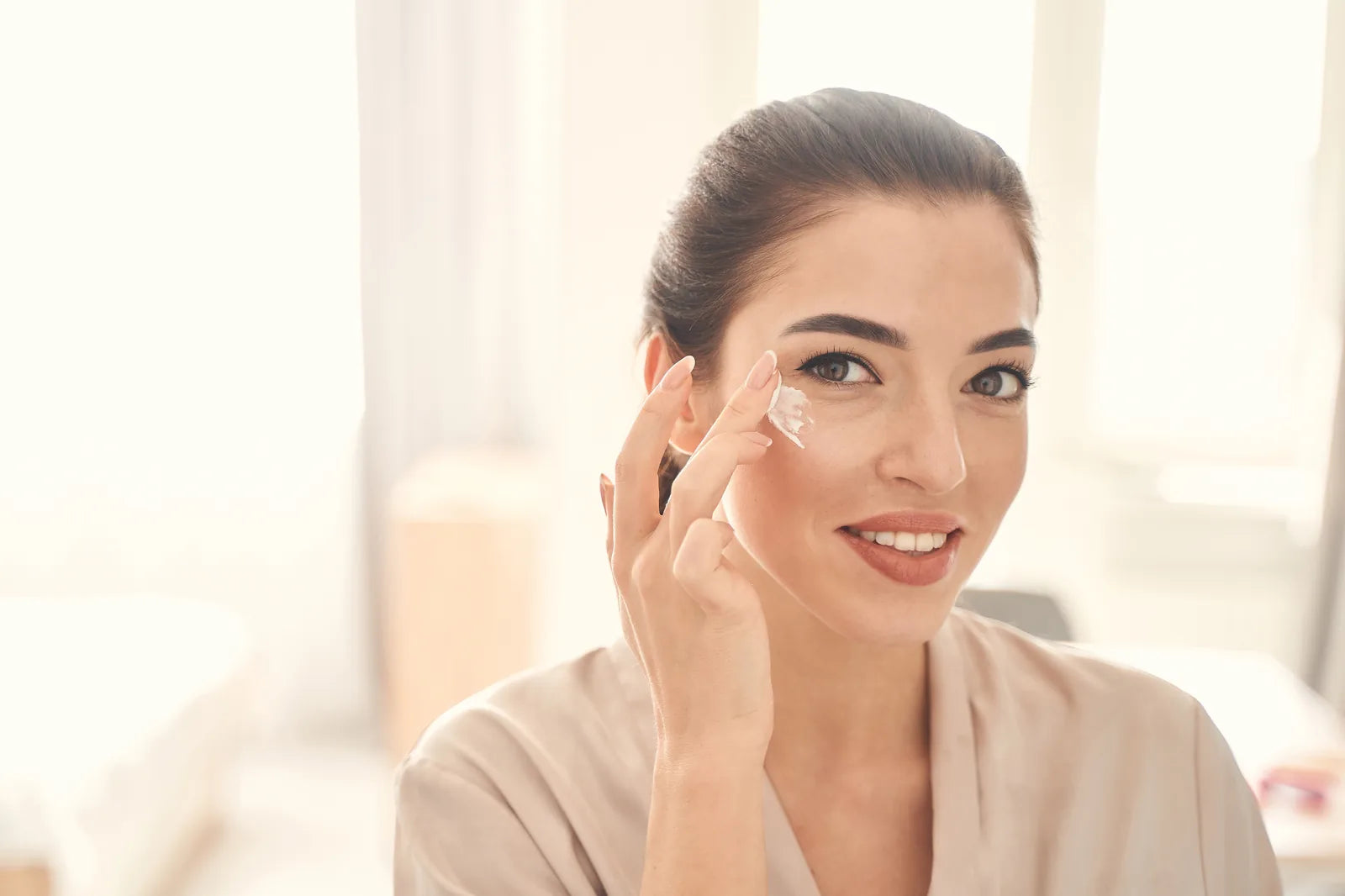 Jeune femme appliquant un soin contour des yeux à la lumière naturelle pour prévenir les premières rides — CAMENYS