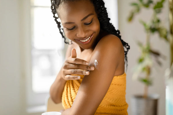 Femme appliquant un soin corps parfumé sur le bras, lumière naturelle chaude, rituel sensoriel